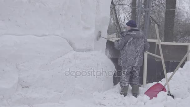 男子铲雪。让雕塑制成的雪。雪雕，块堆等待雕刻。雪雕塑的动物在人工照明。人与雪铲清除在人行道上 — 图库视频影像