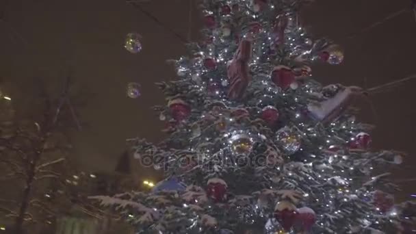 Hermoso árbol de Navidad brillante se encuentra en el medio del parque. Un árbol de Navidad al aire libre en frente de una casa adornada con luces que entran en. Fondo de decoración de Navidad y árbol de Navidad — Vídeo de stock