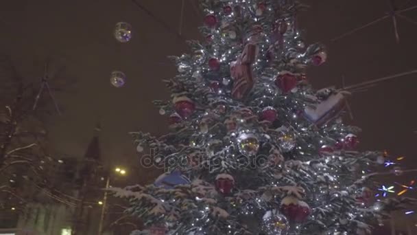 Bela árvore de Natal brilhando fica no meio do Parque. Uma árvore de Natal ao ar livre na frente de uma casa aparada com luzes que entram. Natal decoração fundo e árvore de Natal — Vídeo de Stock