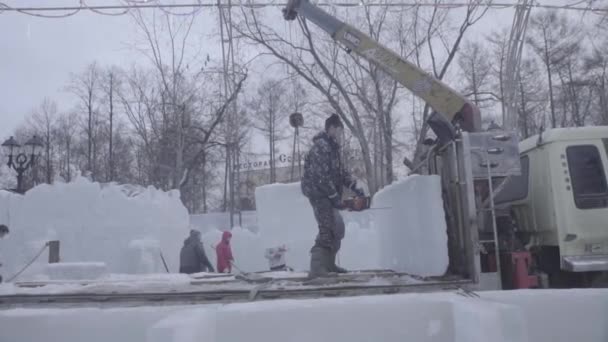 Travailleur utilisant une tronçonneuse sculptant une sculpture sur glace. Les hommes discutent de travail avec des sculptures de glace. Les ouvriers nettoient la neige. Des hommes tirant de la glace. Les travailleurs transportent de la glace et de la neige sur la voiture. Travail avec de la glace et de la neige dans le — Video