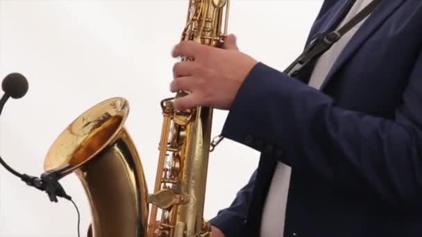 这位音乐家演奏萨克斯管。快乐的萨克斯管吹奏者对 sax 在雅致的套装，白色背景上播放的音乐。新郎手玩萨克斯管。萨克斯管球员在假期的时间。萨克斯管吹奏者。玩的人 — 图库视频影像