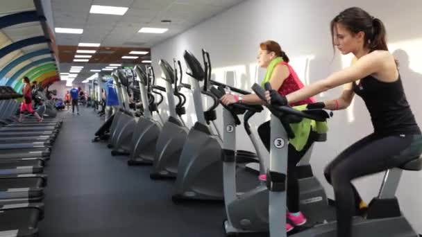 四人在健身房里，锻炼他们的腿做有氧运动训练组。积极女性不同年龄训练对一起做自行车运动在现代健身俱乐部。在健身自行车上的女人 — 图库视频影像