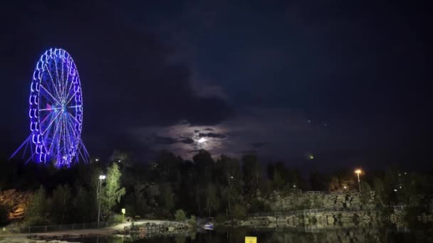 Ruota panoramica la sera al chiaro di luna. Ruota panoramica in luce blu al neon su sfondo scuro, parte della ruota panoramica con illuminazione blu su sfondo nero di notte. timelapse. Una vista di — Video Stock