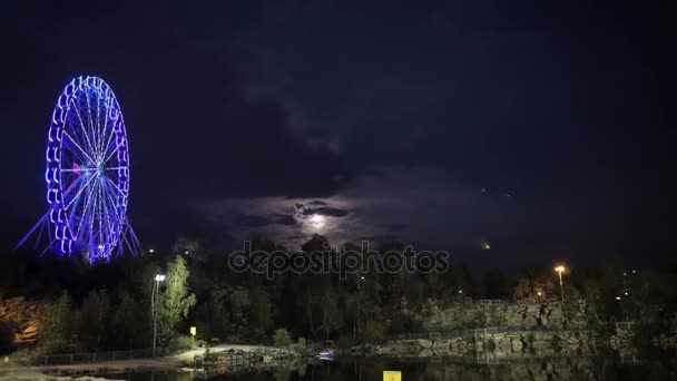 Ruota panoramica la sera al chiaro di luna. Ruota panoramica in luce blu al neon su sfondo scuro, parte della ruota panoramica con illuminazione blu su sfondo nero di notte. timelapse. Una vista di — Video Stock