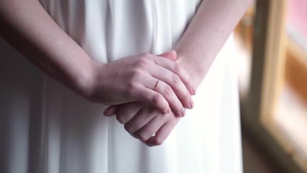 Girl in white dress staying near the window. Girls hand with wedding ring or engagement ring. Beautiful young woman in white dress stay near the window at home.Elegant. Morning of the bride. — Stock Video