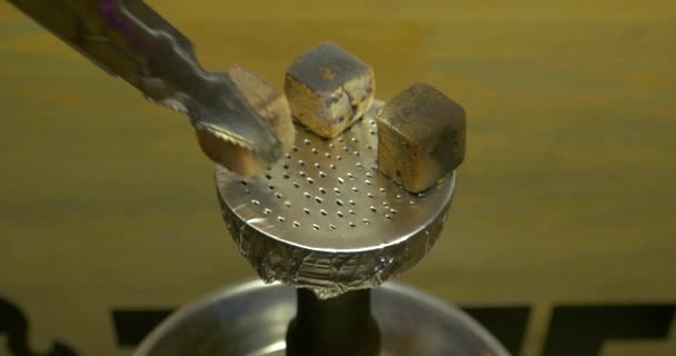 Manns Hand legt brennende Kohlen auf eine Tonschale mit Tabak für Wasserpfeife, Wasserpfeife. Wasserpfeife Thema: Barkeeper hält eine Pinzette mit Kohle für Wasserpfeife und legt sie in eine Tonschale — Stockvideo