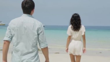 Beyaz giyim şirin çift el plaj gider. Birkaç çalışan ve plaj kıyısında flört genç su yakınında. Onu takip erkek arkadaşının elini tutarak plaj tatil günlerinde yürüyen kadın