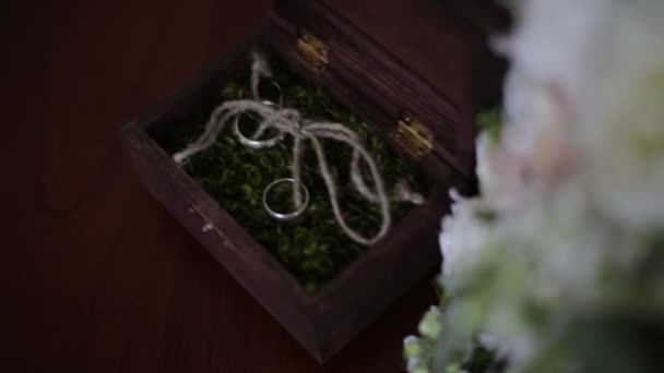 Anillos de boda en una caja de madera llena de musgo sobre la mesa. Caja de madera con anillos de boda se encuentra cerca del ramo de novia de las flores naturales — Vídeos de Stock