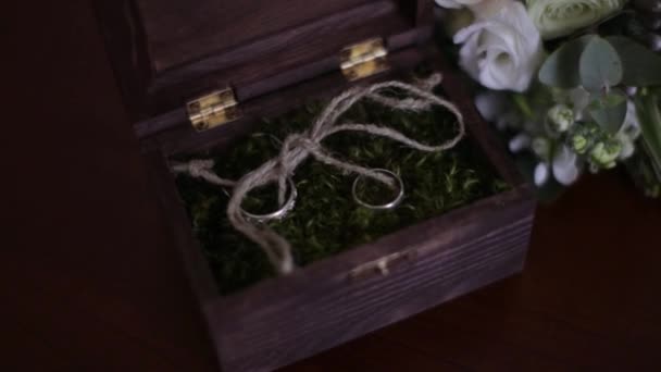 Anillos de boda en una caja de madera llena de musgo sobre la mesa. Caja de madera con anillos de boda se encuentra cerca del ramo de novia de las flores naturales — Vídeo de stock