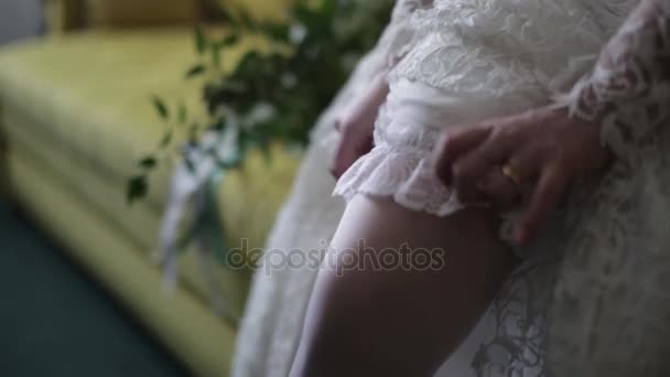 Sposa veste calze a piedi. Sposa di bellezza in un vestito che indossa calze da sposa all'interno. Ritratto femminile bella signora in un vestito. Primo piano delle mani della donna — Video Stock