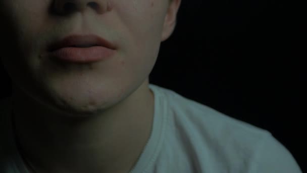 Un tizio con una maglietta bianca che fuma una sigaretta su uno sfondo nero da vicino. il ragazzo fuma su uno sfondo nero — Video Stock