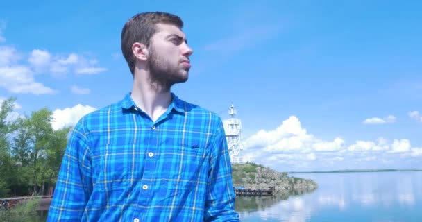 Hombre de pie en la orilla del mar en el clima ventoso, sonriendo y mirando a la distancia. Joven mira a la distancia a través del mar — Vídeo de stock