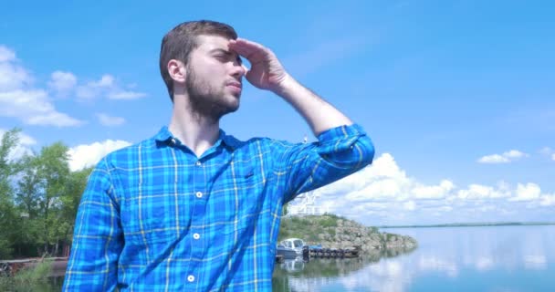 Man standing on the shore of sea at windy weather, smiling and looking into the distance. Young man look into the distance through against the sea — Stock Video