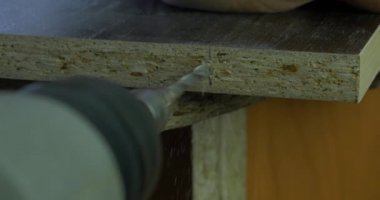 Adam bir tatbikat elinde tutar ve bir delik ahşap bir yönetim kurulu yapar. Ahşap talaşı etrafında uçan. Yakın çekim