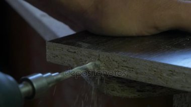 Adam bir tatbikat elinde tutar ve bir delik ahşap bir yönetim kurulu yapar. Ahşap talaşı etrafında uçan. Yakın çekim, yavaş hareket