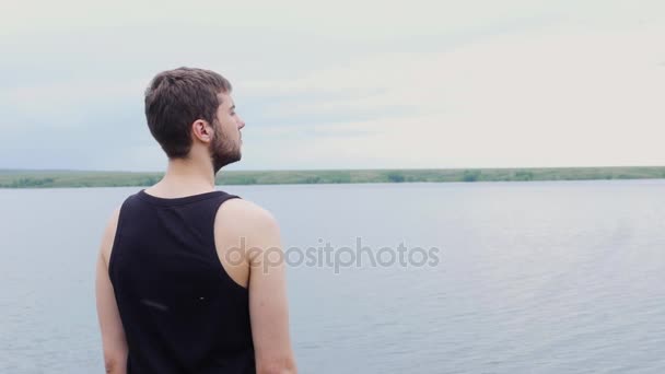 El joven está mirando a lo lejos un lago y montañas. Joven mirando a la distancia del lago — Vídeos de Stock