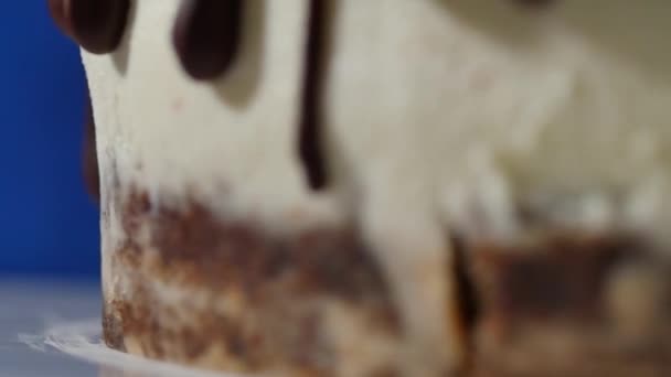 Detail části čokoládový dort s bílými čarami a zmrzlé kapky - potraviny pozadí. Čokoládové proudy izolované na bílém. zblízka čokoládový sirup na dort na tmavě modrém pozadí. — Stock video