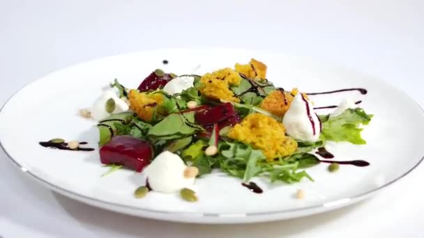 Italian Roast Beet Salad. Salad of roasted beets with goat cheese and pine nuts on white dish isolated on a white background. Tagliatelle with beet and cheese on plate, soft focus — Stock Video