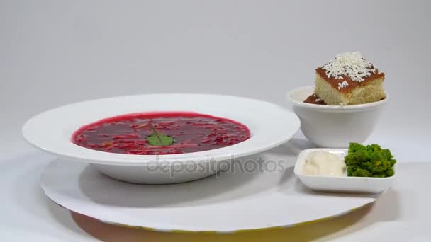 Borsch rojo con carne en plato. Un delicioso borscht rojo con crema agria y hierbas en un plato blanco. Sopa de remolacha tradicional ucraniana - sopa de remolacha roja y albóndigas con ajo — Vídeo de stock