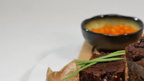 Burro a dadini, caviale, pane nero. Ciotola di caviale rosso con cucchiaio servita con pane a fette, burro ed erbe aromatiche su fondo bianco. Pane integrale, burro e caviale rosso, fondo bianco — Video Stock