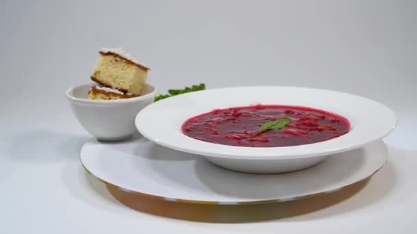 Borsch in plaat met houten lepel en zwart brood geïsoleerd op wit. Groenten en vlees in rode biet soep of borsch met zure room. brood, groene ui, peterselie. — Stockvideo