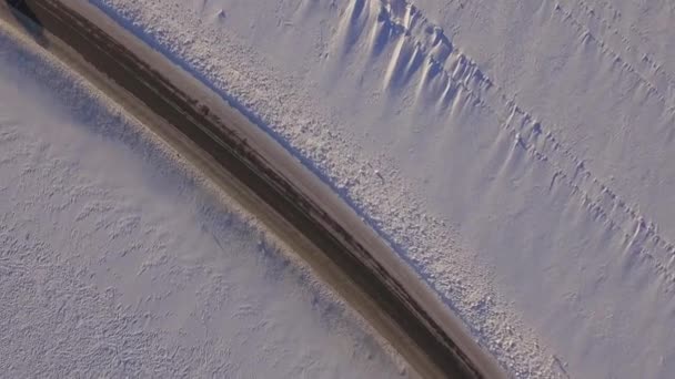 Сув едет по дороге через снежное поле. Вид с воздуха на снежное поле и дорогу с квадрокоптера. Вид с воздуха на заснеженные поля и дорогу — стоковое видео