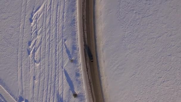 Сув едет по дороге через снежное поле. Вид с воздуха на снежное поле и дорогу с квадрокоптера. Вид с воздуха на заснеженные поля и дорогу — стоковое видео