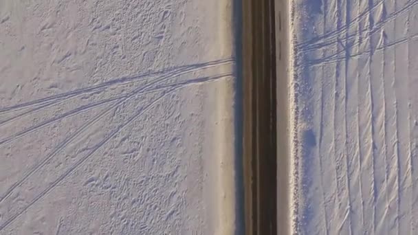 SUV rijdt op weg door de besneeuwde veld. Luchtfoto op een besneeuwde veld en weg van quadrocopter. Luchtfoto van besneeuwde velden en over de weg — Stockvideo