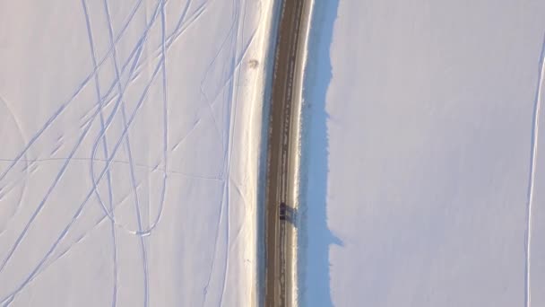 Vista aérea sobre campo nevado y carretera. El coche en la carretera en la tundra, vista superior — Vídeo de stock