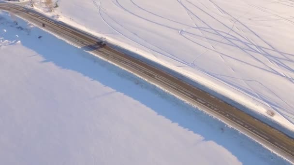 Vista aérea sobre campo nevado y carretera. El coche en la carretera en la tundra, vista superior — Vídeos de Stock