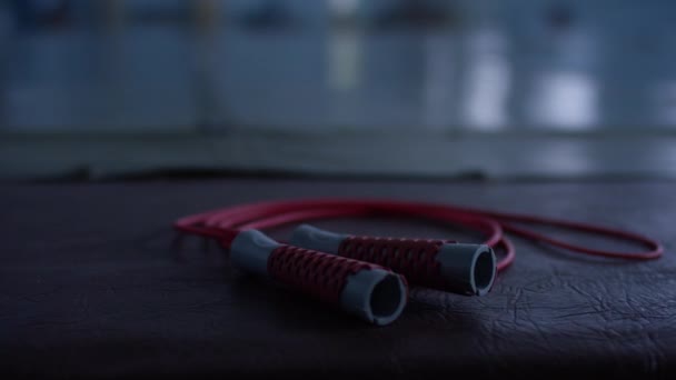 Corde à sauter rouge avec poignées noires sur un sol de gymnase noir, gros plan — Video