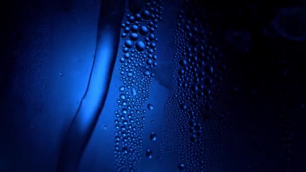 Uma gota de água em uma macro close-up de vidro com bokeh espumante no fundo azul turvo. Abstrato gota de água. Raindrop deslize para baixo do vidro da janela, formando figura abstrata — Vídeo de Stock