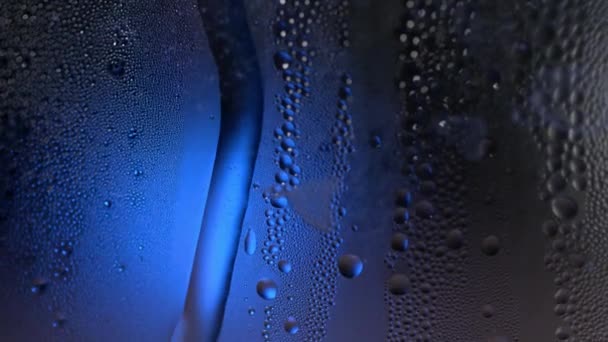 Una gota de agua en un macro de primer plano de vidrio con bokeh brillante sobre fondo borroso azul. Abstracto gota de agua. Gota de lluvia deslizarse por el vidrio de la ventana, formando figura abstracta — Vídeo de stock