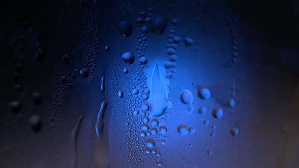 En droppe vatten på ett glas närbild makro med gnistrande bokeh på blå suddig bakgrund. Abstrakta droppe vatten. Regndroppe glida ner fönsterglas, bildar abstrakta figur — Stockvideo