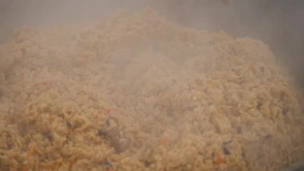 Cozinhar prato pilaf uzbeque ao ar livre com carne de vaca em panela de caldeirão de metal grande. Refeições culinárias. Pilaf em um caldeirão, comida de rua de perto — Vídeo de Stock