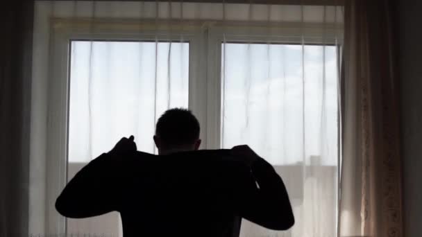 Silhouet van elegante luxe jongeman gelegd op zijn jasje in hotelkamer met venster op een achtergrond — Stockvideo