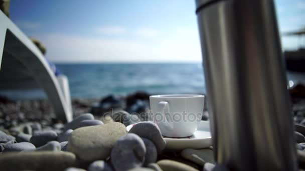 Uma chávena de café com mar azul. Taça branca nas rochas na costa — Vídeo de Stock
