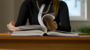 Kadın bir kitap aracılığıyla leafing eller. Kitap aracılığıyla leafing masada oturan kadın