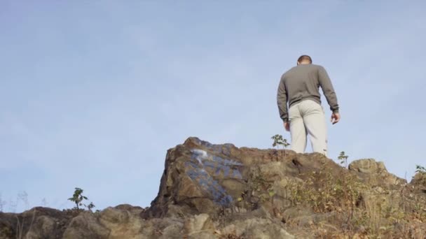 Mannelijke atleet ontspannen na de training terwijl staande op stenen rock tegen hemel achtergrond achteraanzicht. Mannelijke sporters op de rots — Stockvideo