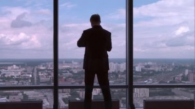 İşadamı büyük penceresinden bir ofis binasının yanında duran ve saatine geri görüntülemek kontrol takım elbiseli. Onun kol saati görünümlü pencere ayakta işadamı