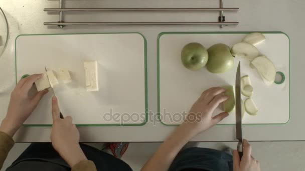 Чайлдс режет яблоко и сыр вид сверху. Дети маленькая девочка и мальчик готовят на кухне — стоковое видео