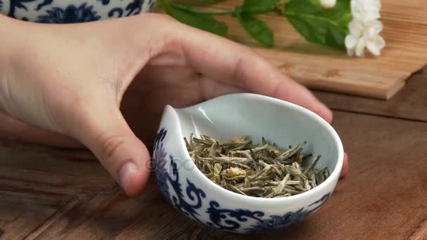 Teiera di vetro con fiore di tè in fiore all'interno sullo sfondo di legno cinese foglie di tè verde da vicino nella tazza tradizionale. cerimonia del tè. Tè cinese, cerimonia — Video Stock