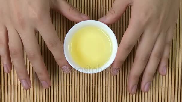 Tangan womans memegang cangkir putih teh Cina bambu latar belakang, atas pandangan. Seorang wanita memegang secangkir teh. teh sencha hijau jepang di bunga mug — Stok Video