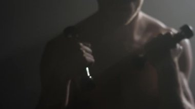 Savaşçı trenlerle dilsiz çanları. Sporcu trenler ve dumbbells ile egzersizleri yapın. Seksi kaslı adam
