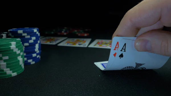 Pessoa a mostrar o seu baralho no jogo de poker. Jogador de cartas verifica sua mão, dois ases em, fichas em segundo plano na mesa de jogo verde, foco em cartão. Mão de dois ases no poker — Fotografia de Stock