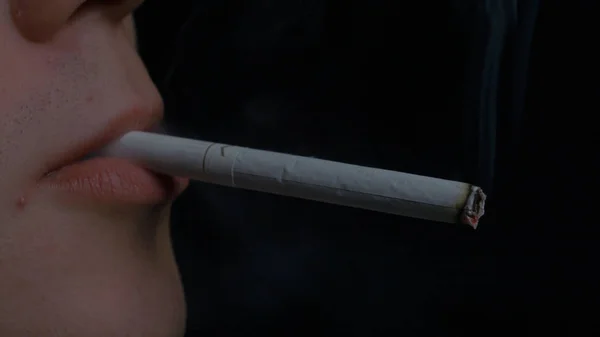 Man smoking cigarette on black background. Close up portrait of young man smoking cigarette. Smoking. A young man smoking a cigarette — Stock Photo, Image