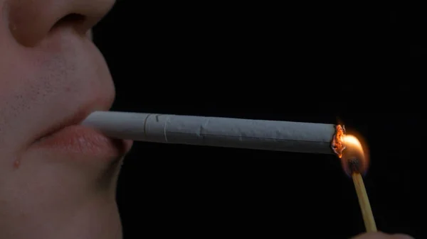 Uomo che fuma sigarette su sfondo nero. Ritratto ravvicinato di un giovane che fuma sigarette. Fumo. Un giovane che fuma una sigaretta — Foto Stock