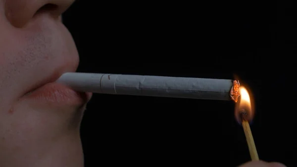 Man smoking cigarette on black background. Close up portrait of young man smoking cigarette. Smoking. A young man smoking a cigarette