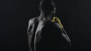 Kaslı adam siyah arka plan üzerine boks dikiz. Gölge boks pratik Afro Amerikan genç erkek boxer. Sarı boks eldivenleri boksör