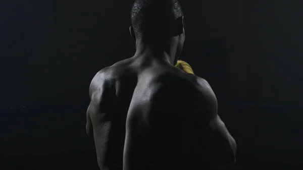 Πίσω όψη του μυώδης άνδρας πυγμαχία σε μαύρο φόντο. Αφρο αμερικανικό νεαρό αρσενικό μπόξερ εξάσκηση σκιαμαχία. Μπόξερ σε κίτρινα γάντια του μποξ — Φωτογραφία Αρχείου